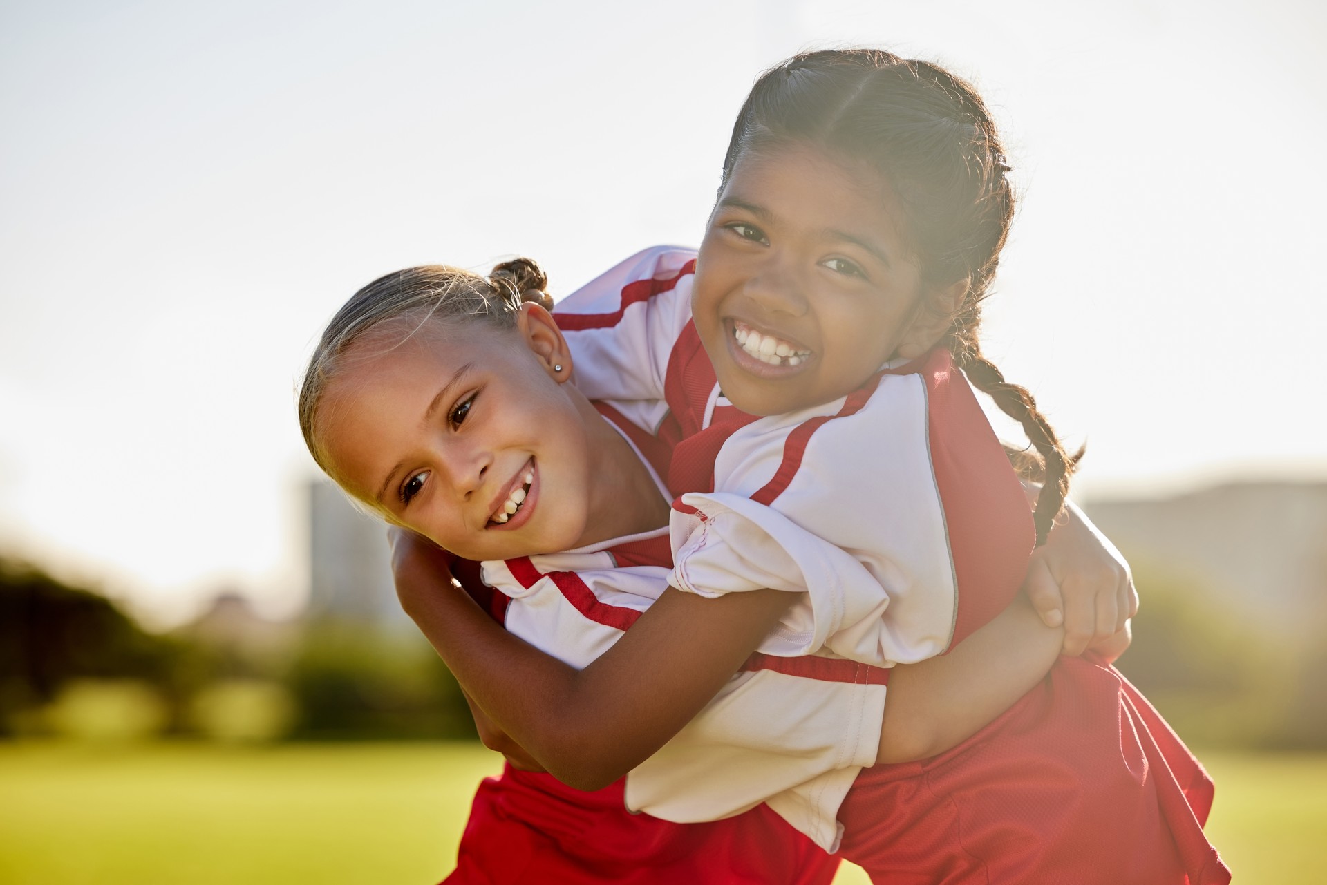 Girl football players, children hug and smile after sports training match for competition. Young football friends, embrace after game and learning collaboration and teamwork together while exercising